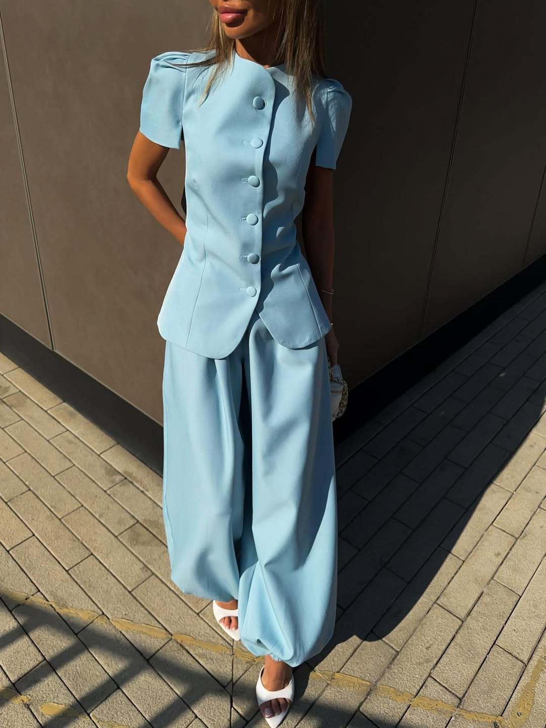 Powder blue short-sleeve peplum jacket and wide-leg trouser set worn full length against a dark wall