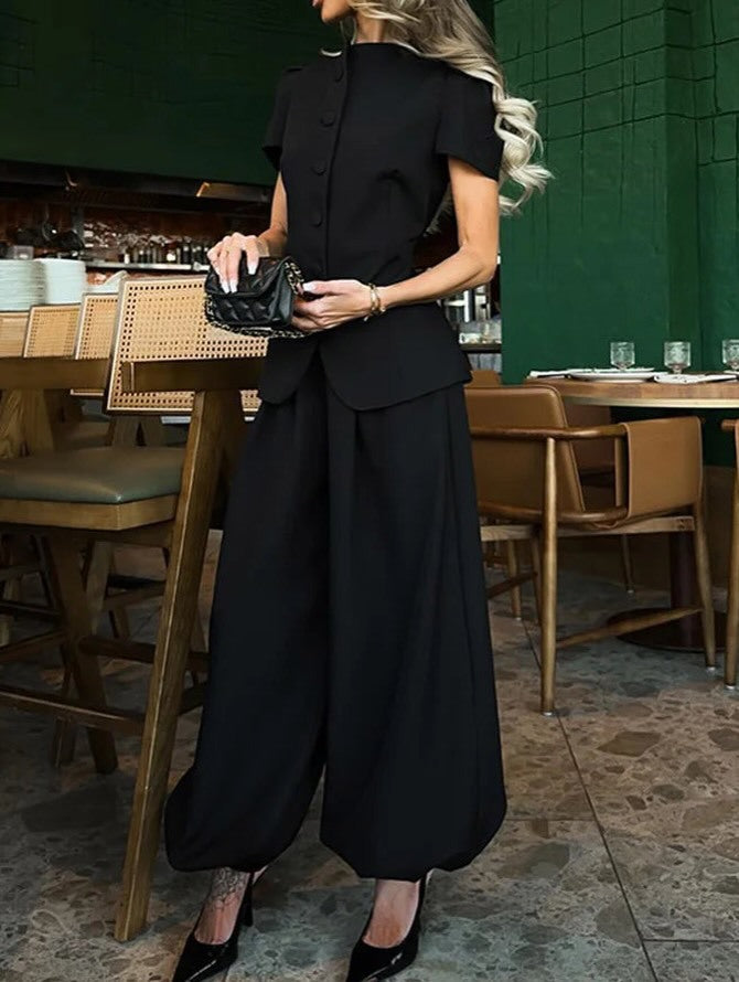 Black peplum jacket and wide-leg trousers worn seated at a counter